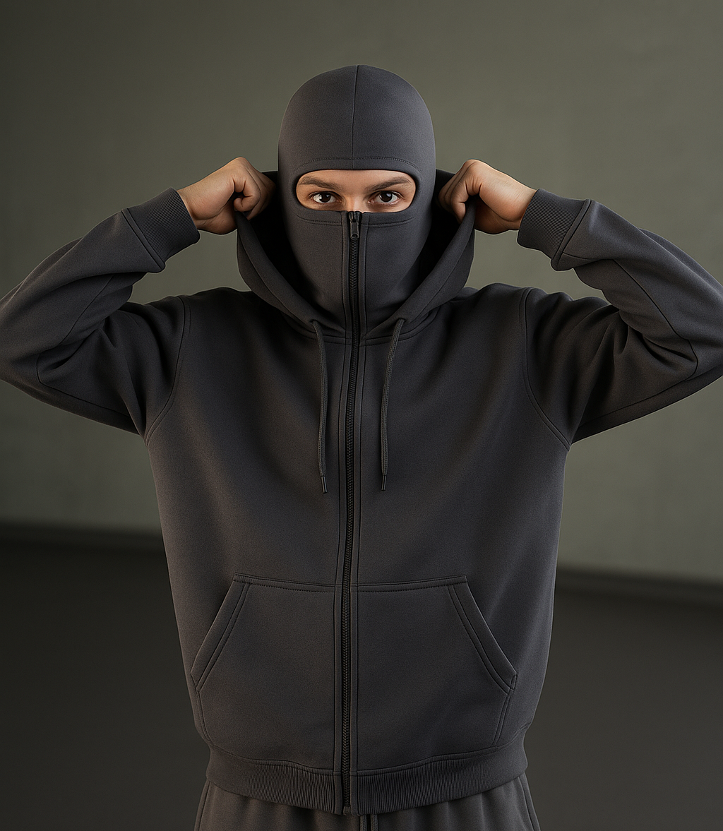 Person wearing a grey hoodie and pants with a hood on a dark background