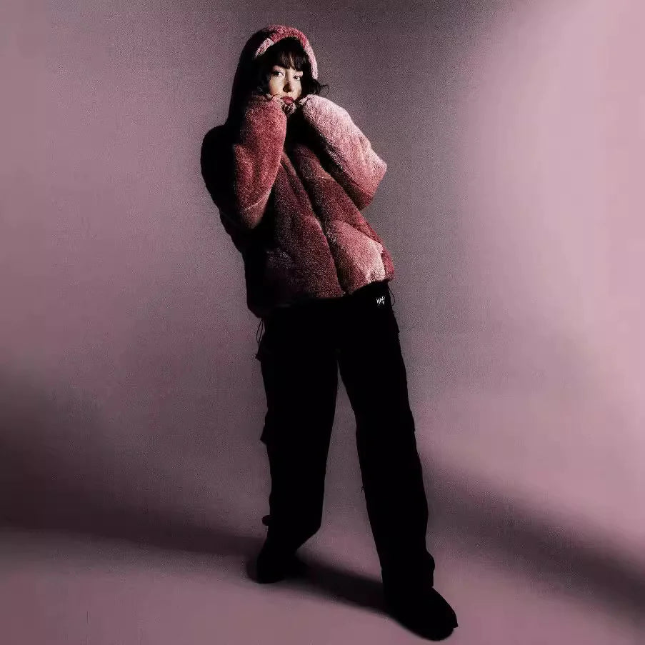 Person wearing a pink fuzzy hoodie and black pants against a purple background