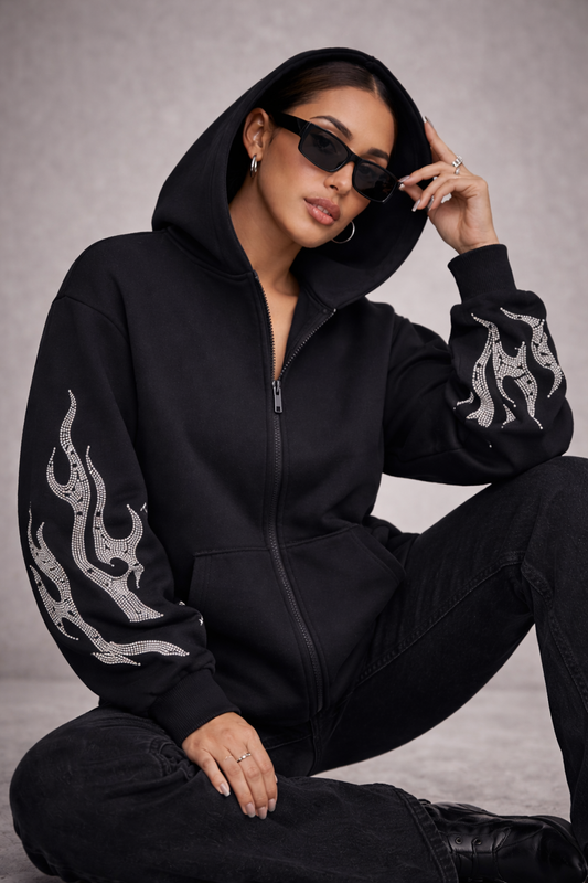 Person wearing a black hoodie with flame designs on sleeves against a neutral background