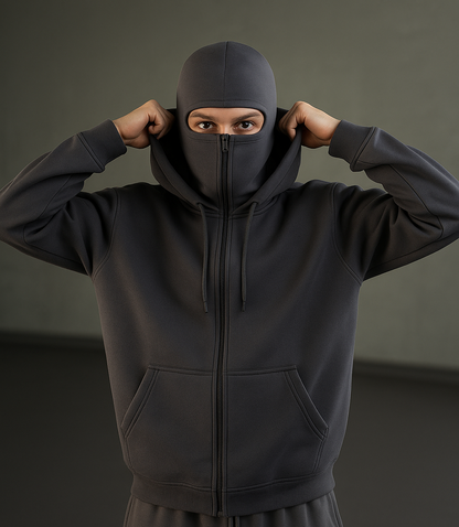 Person wearing a grey hoodie and pants with a hood on a dark background
