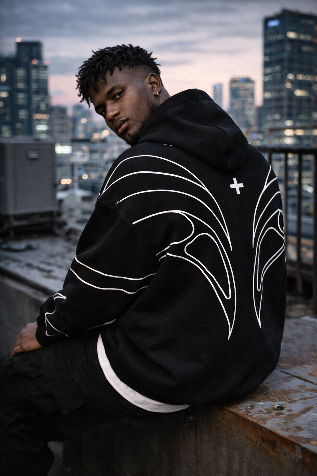 Person wearing a black hoodie with white designs on a rooftop at dusk.