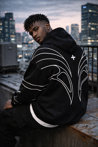 Person wearing a black hoodie with white designs on a rooftop at dusk.